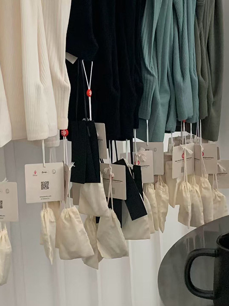 Seamless knitwear samples in ivory and black, hanging with branded hang tags and cotton dust bags at Cawoolyang showroom